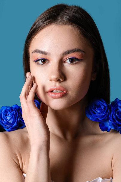 Beautiful young woman with blue roses on color background - Photo, Image