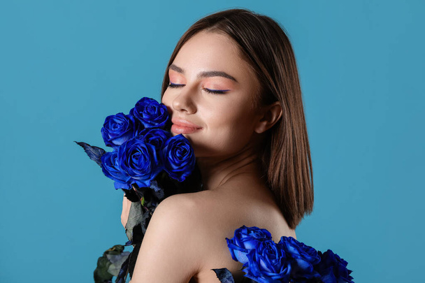 Beautiful young woman with blue roses on color background - Foto, imagen