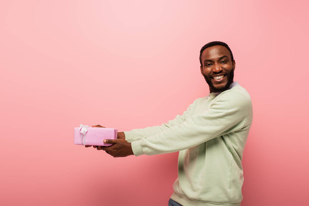 allegro uomo afro americano in possesso di dono in mani tese su sfondo rosa - Foto, immagini