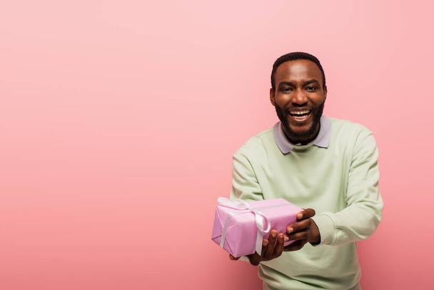 alegre afroamericano hombre mostrando presente aislado en rosa - Foto, Imagen