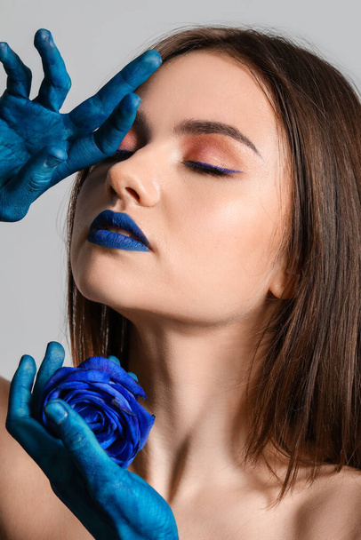 Stílusos fiatal nő festett kézzel és kék rózsa szürke háttér - Fotó, kép