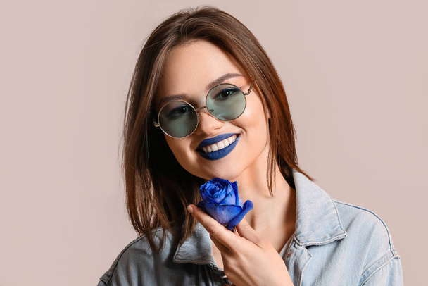Stylish young woman with blue rose on grey background - Foto, imagen