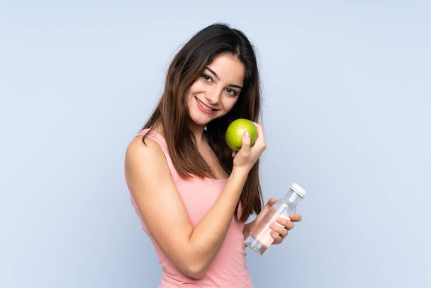 Молода біла жінка ізольована на синьому фоні з яблуком і пляшкою води
 - Фото, зображення