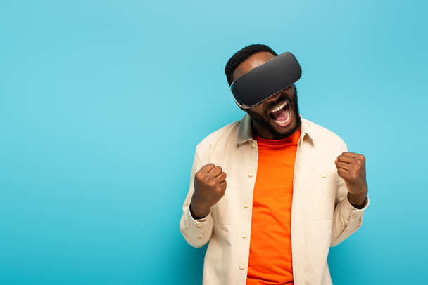 excited african american man in vr headset showing rejoice gesture isolated on blue - Foto, Imagem