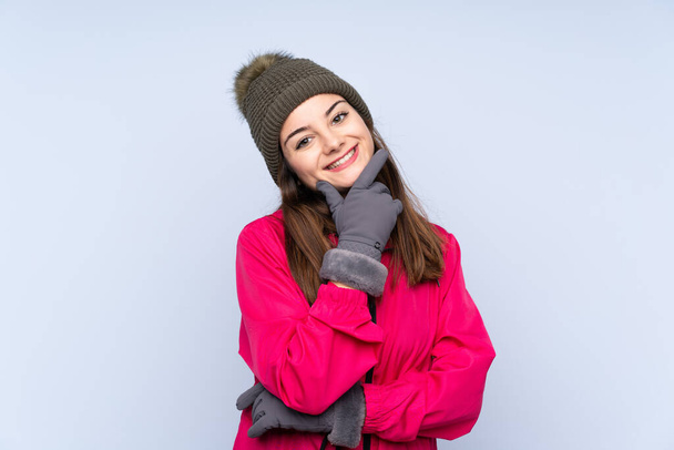 Νεαρή κοπέλα με χειμερινό καπέλο απομονωμένη σε μπλε φόντο χαμογελώντας - Φωτογραφία, εικόνα