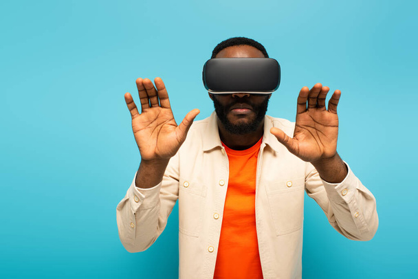 african american man in vr headset touching something isolated on blue - 写真・画像