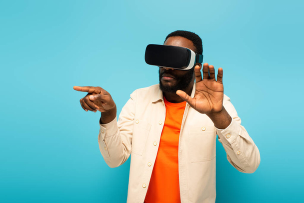 african american man in vr headset pointing with finger while touching something isolated on blue - Valokuva, kuva