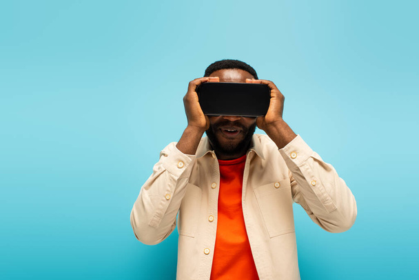 african american man touching vr headset while gaming isolated on blue - Photo, Image