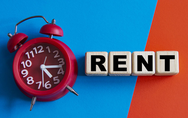 RENT - word on wooden cubes on a multi-colored background with a red alarm clock. Business concept - Фото, зображення
