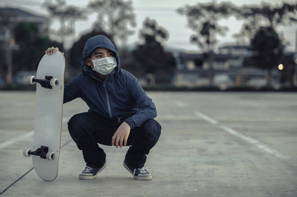 Fáradt ázsiai gyerek visel védő arc maszkok Ül a szabadban gördeszka, gördeszkások az utcán tartja a társadalmi távolságot, míg a Coronavirus járvány., Tartsa az egészséges életmód. - Fotó, kép