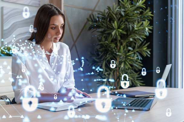 Attractive businesswoman in white shirt at workplace working with laptop to defend customer cyber security. Concept of clients information protection. Padlock hologram over office background. - Фото, зображення