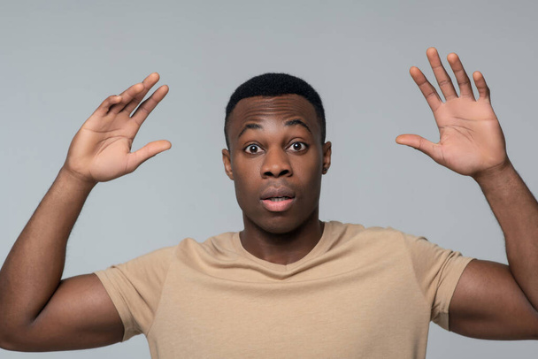 Surprised young man with raised arms gesturing - Foto, afbeelding