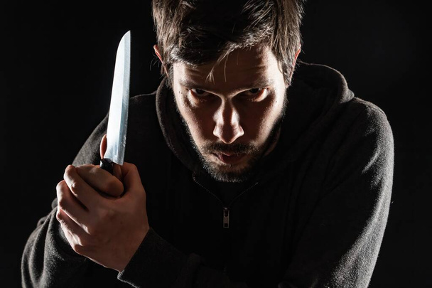 Maníaco aterrador y malvado o asesino con cuchillo sobre fondo negro. - Foto, Imagen