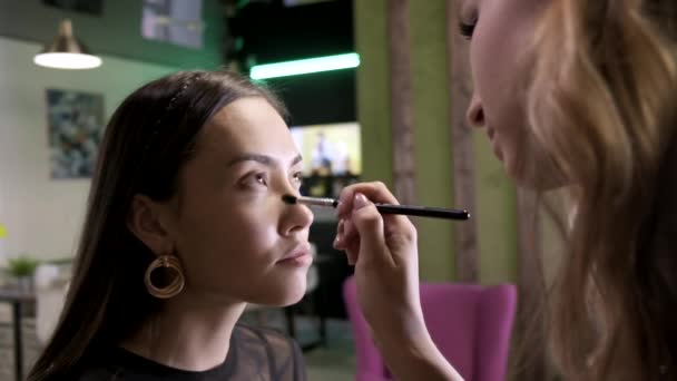 artista maquiagem aplica creme tom base no rosto meninas usando escova no salão de beleza - Filmagem, Vídeo