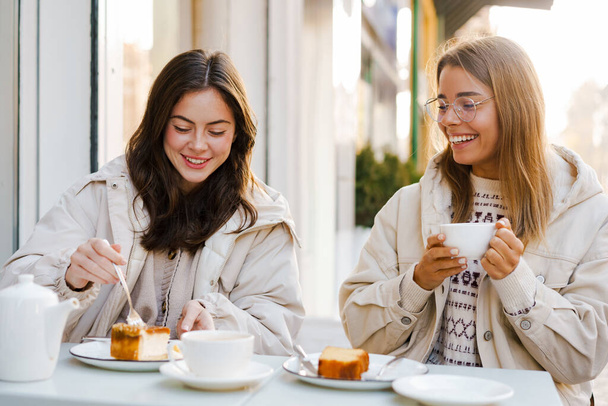 Two cheerful attractive women friends having tea and cakes at the cafe outdoors - Photo, image