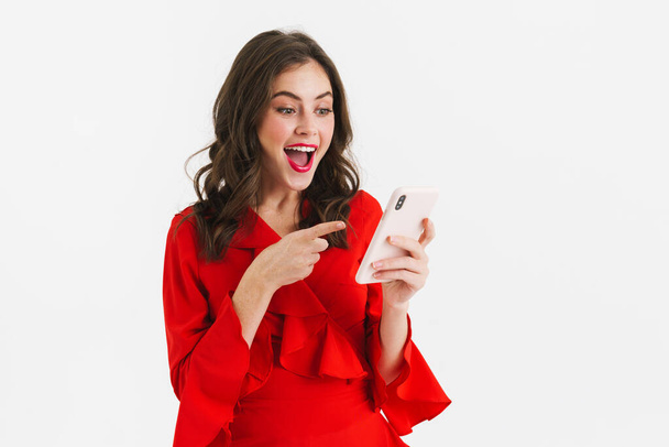 Cheerful young woman in red dress using mobile phone isolated over white background - Φωτογραφία, εικόνα