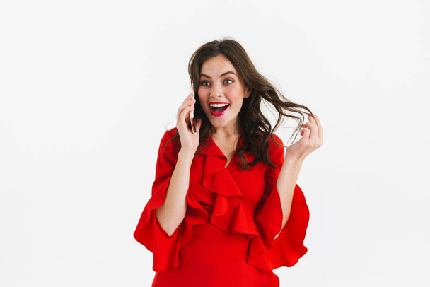 Cheerful young woman in red dress using mobile phone isolated over white background, calling - Foto, imagen