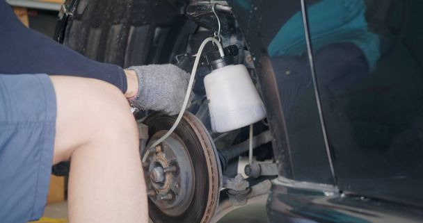 Auto mechanic replacing brake fluid on a vehicle, technician bleed air out of disc brake system in garage workshop, Car repair in a car service - Fotografie, Obrázek