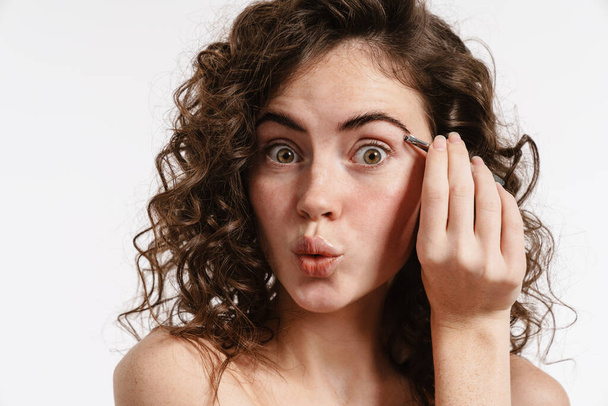 Half-naked surprised woman plucking her eyebrows with tweezer isolated over white background - Valokuva, kuva
