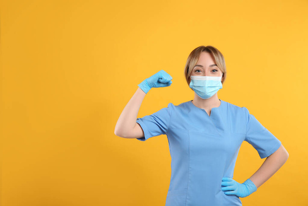 Doctor with protective mask showing muscles on yellow background, space for text. Strong immunity concept - Foto, imagen