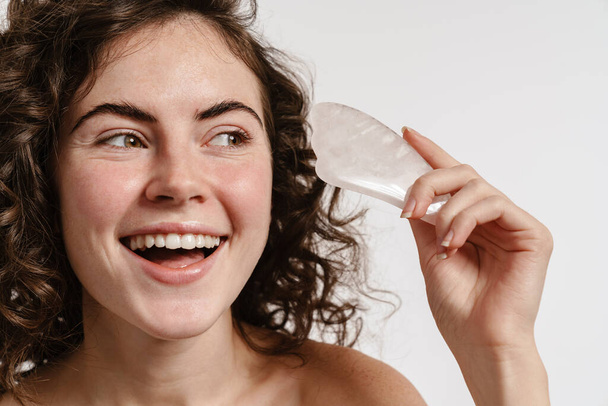 Happy shirtless girl smiling while posing with gua sha stone isolated over white background - Фото, изображение