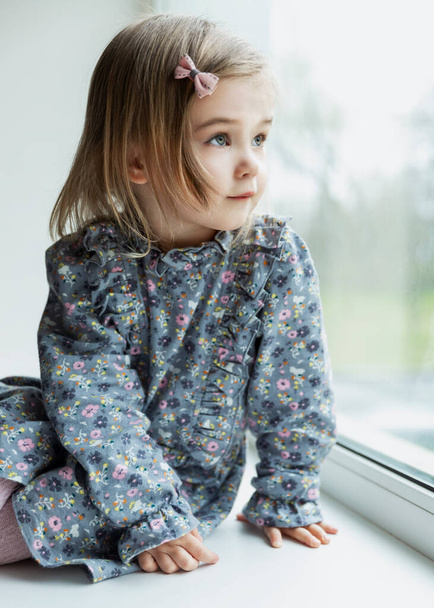 Smiling cute little girl looks out the window. Close-up. Vertical. - Foto, imagen