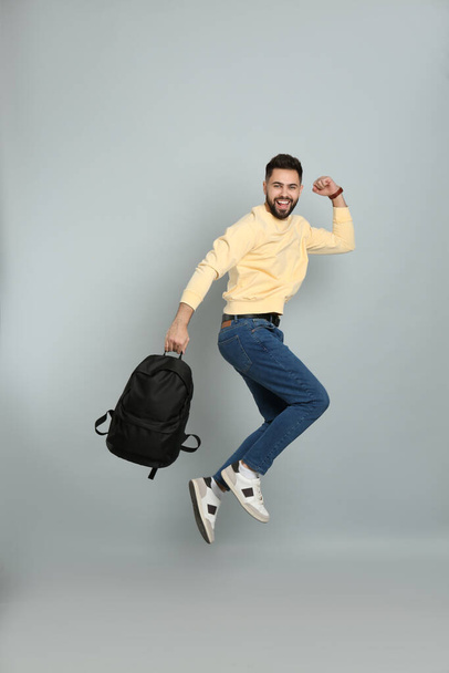 Emotional man with stylish backpack jumping on light grey background - Foto, Imagem