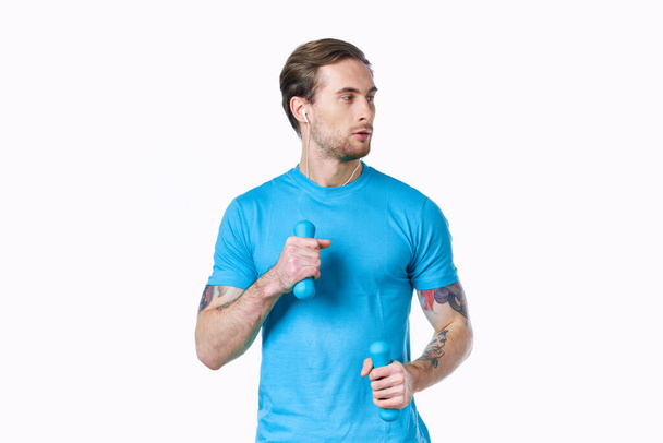 Mann mit Hanteln in blauem T-Shirt auf hellem Hintergrund mit Blick auf den seitlichen Ausschnitt - Foto, Bild