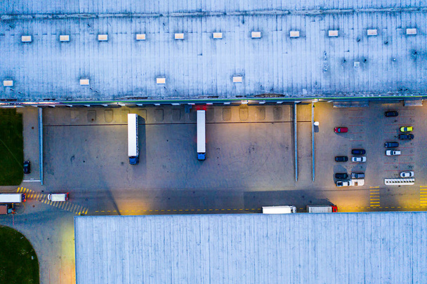 Aerial view of goods warehouse Night. Logistics center in industrial city zone from above. Aerial view of trucks loading at logistic center - Photo, Image