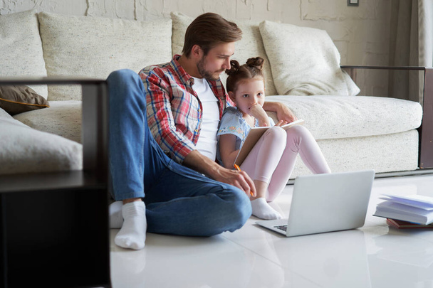 Smiling father and daughter sitting on floor in living room with laptop, teaching lessons - Φωτογραφία, εικόνα