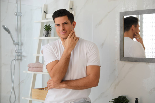 Handsome man touching his smooth face in bathroom after shaving - Fotó, kép