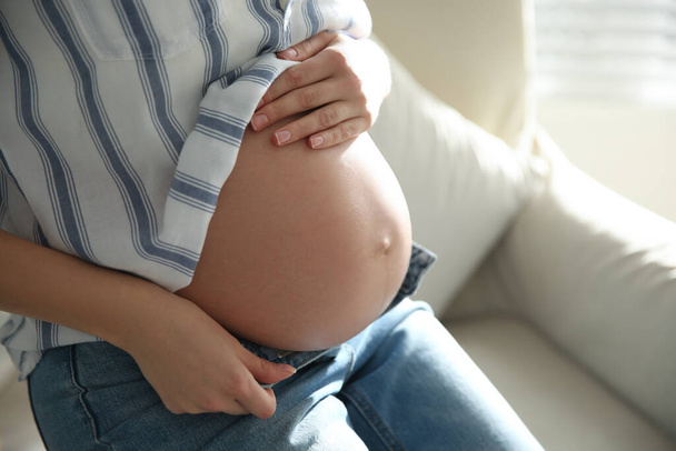 Pregnant woman touching her belly indoors, closeup - Foto, afbeelding