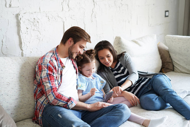 Beautiful young family with little child taking a selfie with a smartphone at home on the couch - Foto, Bild