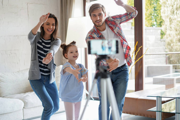 Χαρούμενη νεαρή οικογένεια χορεύει στο σπίτι με τη μικρή χαριτωμένη κόρη του, τραβώντας βίντεο - Φωτογραφία, εικόνα