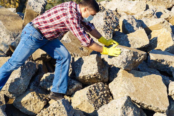 un hombre trabaja con un montón de piedras y pedazos rotos de hormigón, lleva escombros de construcción - Foto, Imagen