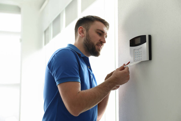 Homme installant le système de sécurité à domicile sur le mur blanc dans la chambre - Photo, image