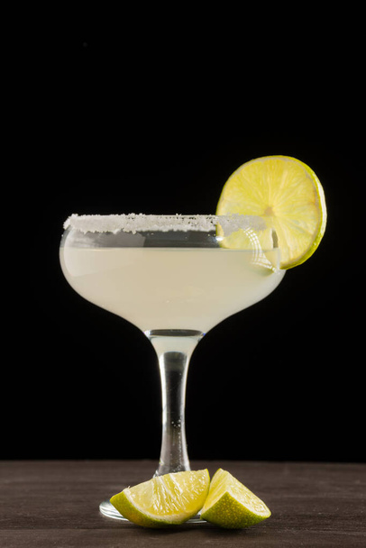 View of margarita cocktail glass with cut limes, on wooden table, vertical black background, with copy space - Fotó, kép