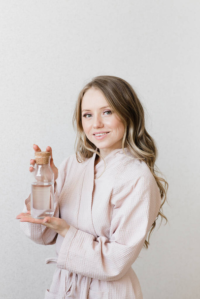 a girl in a pink robe holds a glass bottle with water in her hands natural cosmetics natural beauty - 写真・画像
