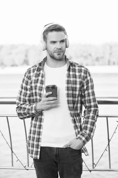 young man student in casual shirt and headset listen ebook and music drink fresh aromatic coffee while walking outdoor, daily routine - 写真・画像