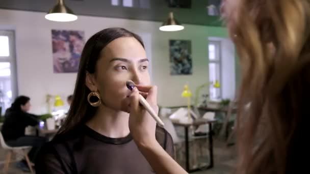 makeup artist applies base tone cream on girls face using brush in beauty salon - Footage, Video