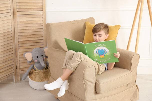 Little boy reading book in armchair at home - Foto, afbeelding