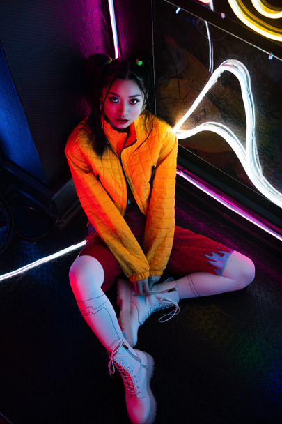 high angle view of young asian woman in bright clothing sitting on floor and looking at camera - Foto, immagini