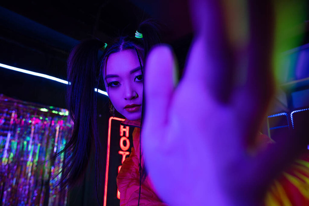 молода азіатська жінка з розмитою рукою біля неонового знака з готельним випуском надворі
  - Фото, зображення