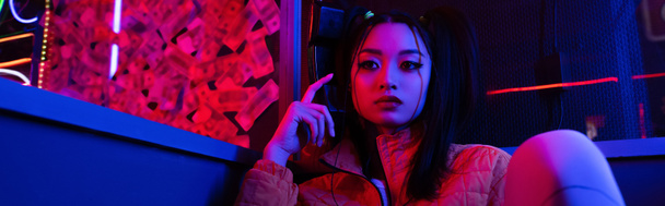 young asian woman looking away near neon lighting, banner - 写真・画像