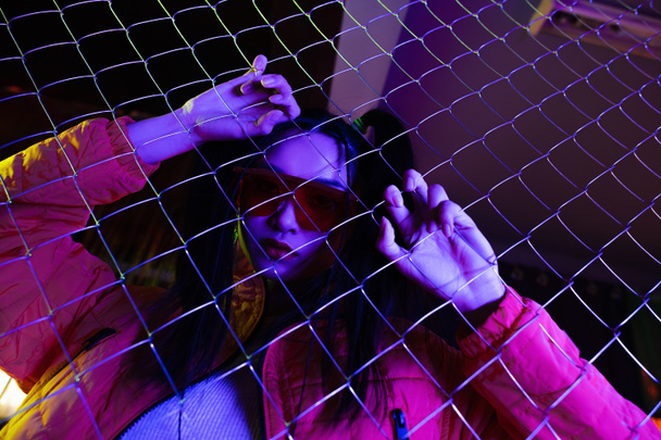 low angle view of trendy young asian woman in sunglasses near metallic fence  - Foto, Imagem