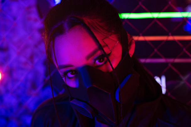 neon lighting on young asian woman in gas mask looking at camera - 写真・画像
