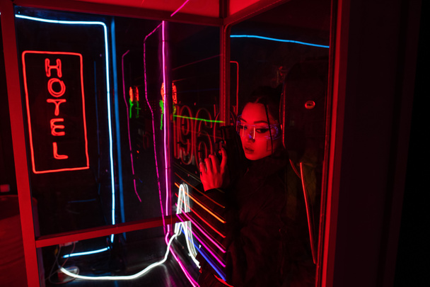 armed asian woman in sunglasses holding gun near neon hotel sign  - Fotoğraf, Görsel