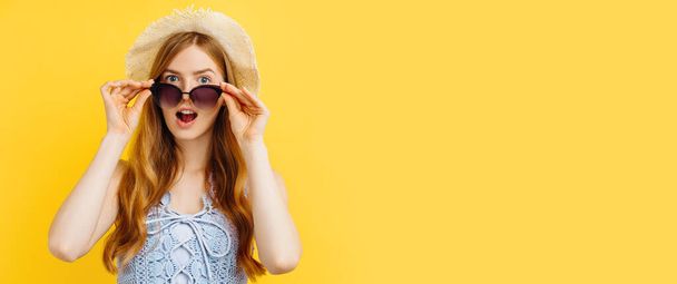 Portrait of surprised young summer woman in hat holding hands near open mouth over isolated yellow background - Photo, image