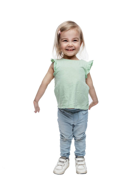Smiling little girl 2 years old in jeans stands. Happiness and love. Full height. Isolated on white background. Vertical. - Photo, Image