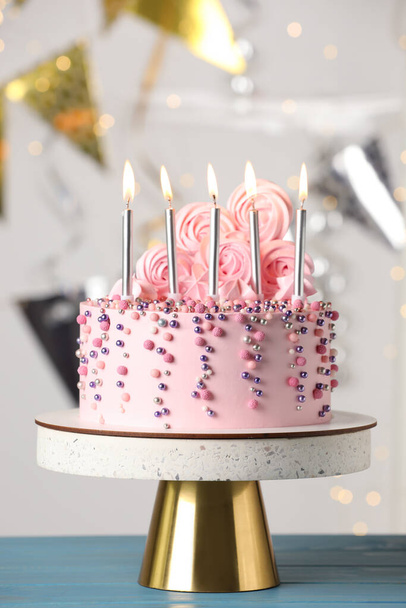 Krásně zdobený narozeninový dort na tyrkysovém dřevěném stole proti rozmazaným slavnostním světlům - Fotografie, Obrázek